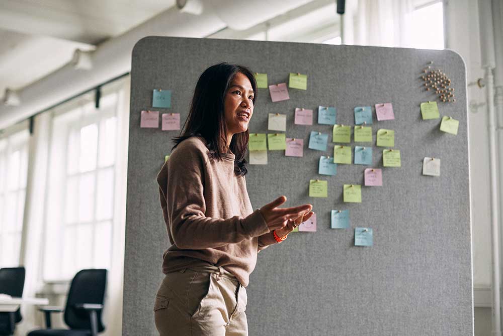 En affärskvinna står framför en grå anslagstavla med postitlappar