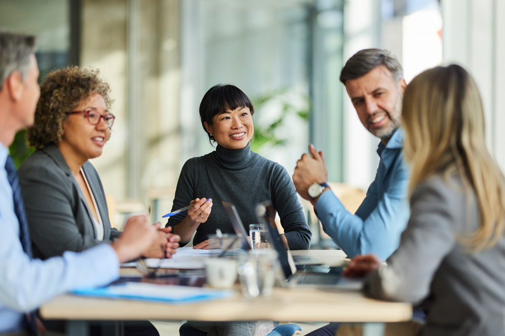 En grupp glada multietniska entreprenörer och affärspersoner kommunicerar under ett affärsmöte på ett modernt kontor.